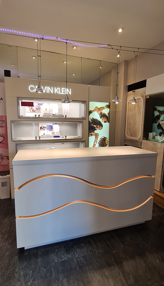 Banque d’accueil sur mesure pour bijouterie à Alès, design contemporain avec vagues dorées éclairées et finition texturée