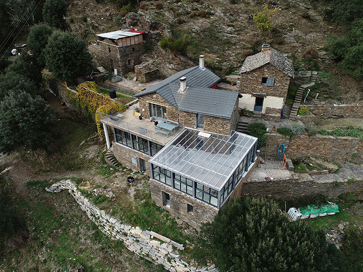 Vue aérienne d’une maison en pierre rénovée avec extension moderne vitrée et couverture de piscine, projet d’architecte d’intérieur dans les Cévennes